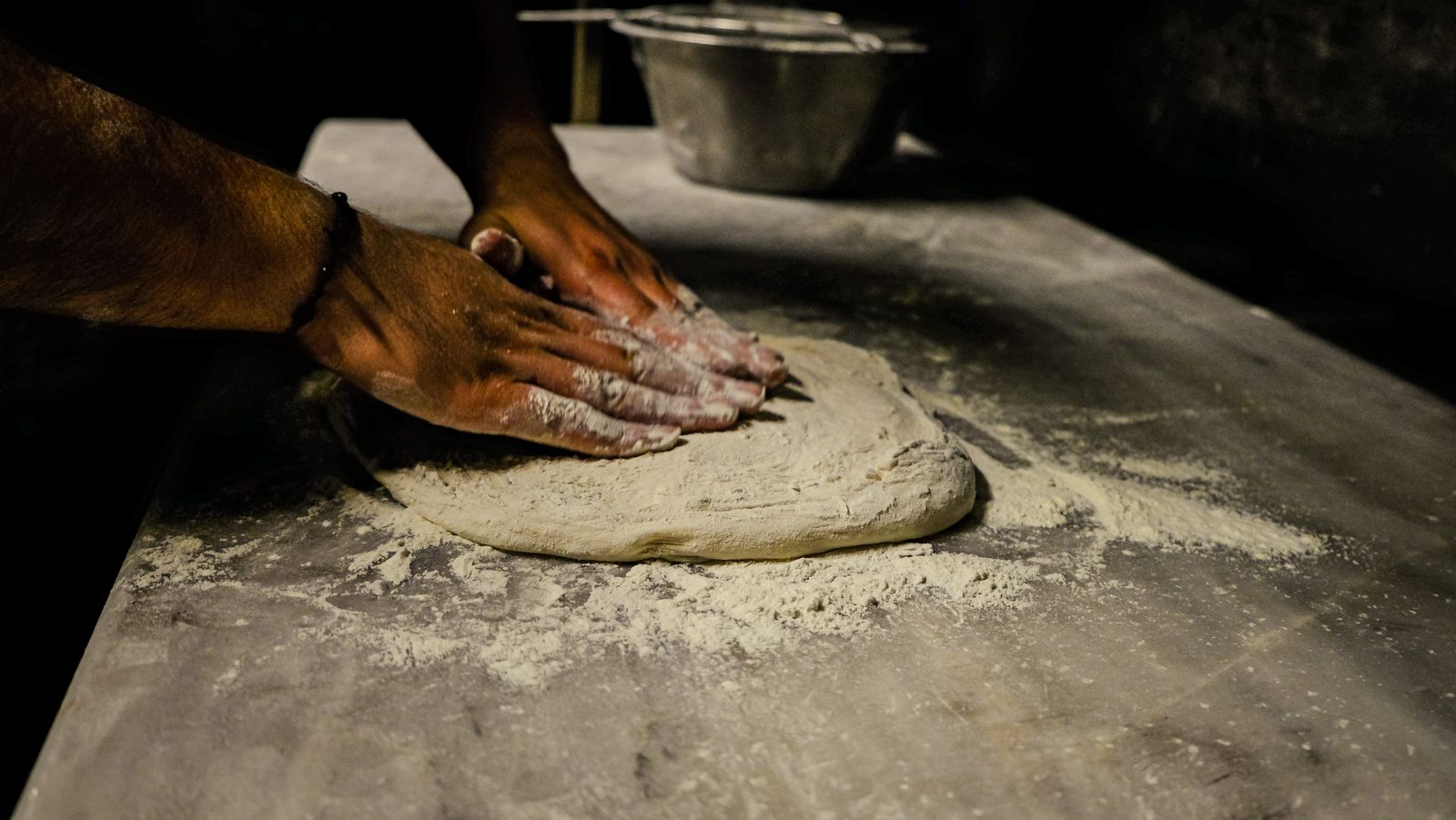 Des mains pétrissent une pâte à focaccia sur un plan de travail fariné