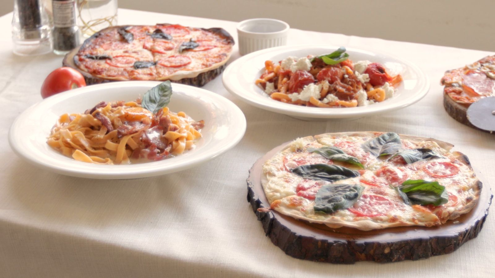 Une table dressée avec pâtes, pizza et tomates fraîches